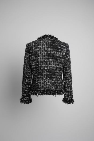 A close-up of a black and white tweed fabric with fringed trim hanging against a grey background.
